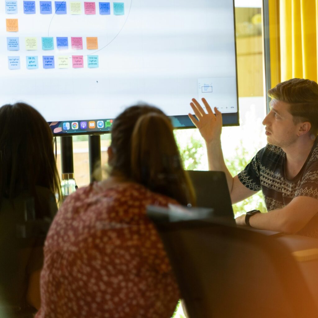 Teammeeting mit digitalem Whiteboard: Mitarbeitende diskutieren gemeinsam Projektideen, analysieren Inhalte auf einem Bildschirm und entwickeln Lösungen in einem modernen Besprechungsraum.