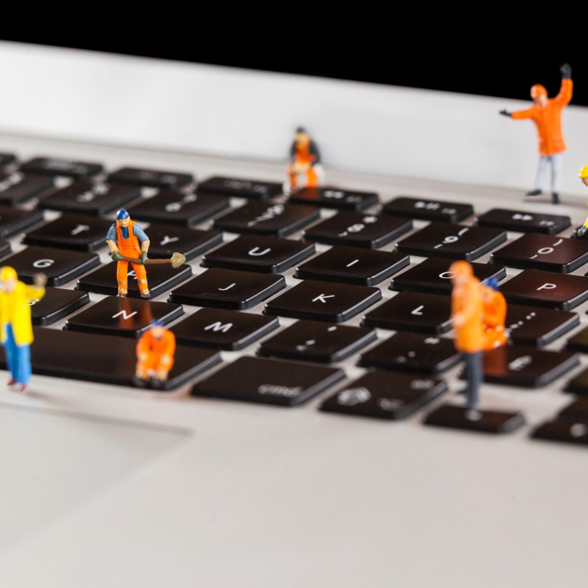 Conceptual image of miniature workmen repairing a laptop keyboard